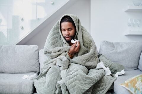 A man wrapped in a blanket highlights the importance of self-care for those with chronic sinusitis.
