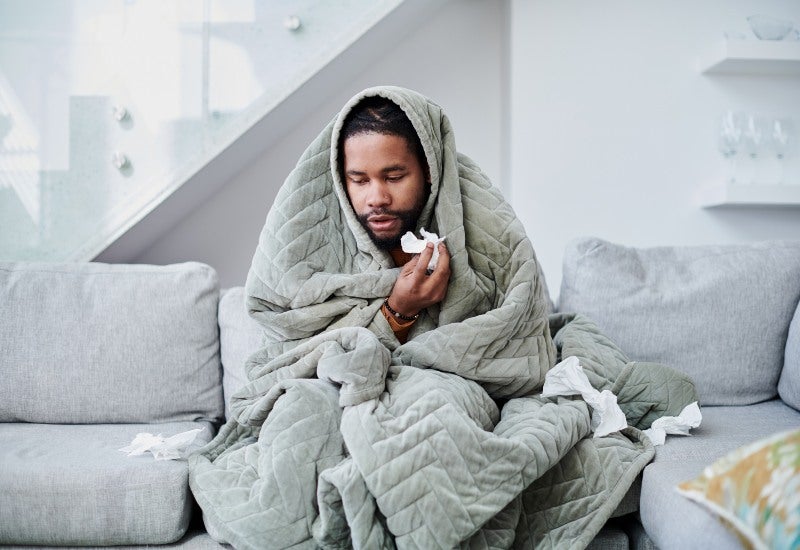 A man wrapped in a blanket highlights the importance of self-care for those with chronic sinusitis.
