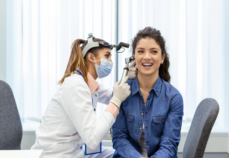 A female doctor wearing a mask examines a young woman's ear for Tinnitus Treatment in Jupiter, FL