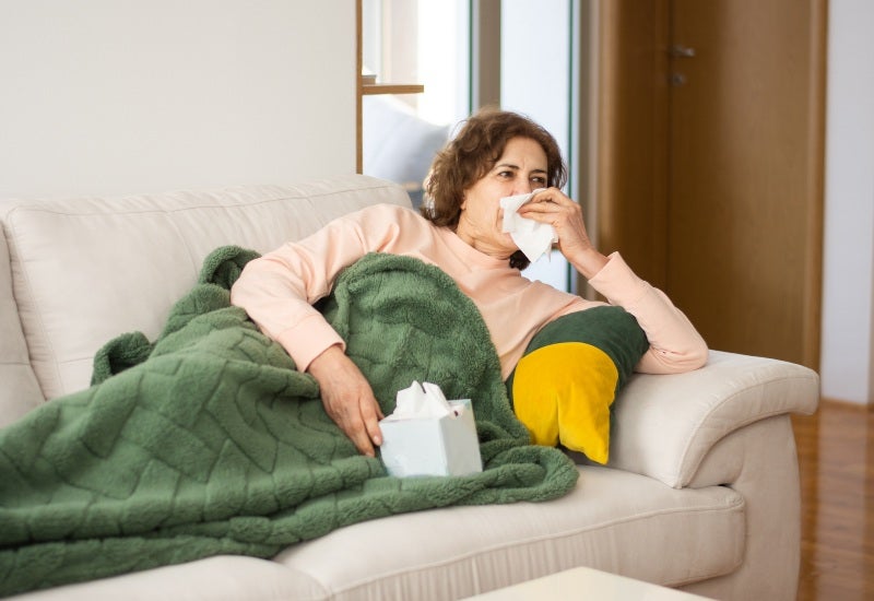 A woman with cold symptoms, sitting on a sofa with a green blanket, in Jupiter, FL.