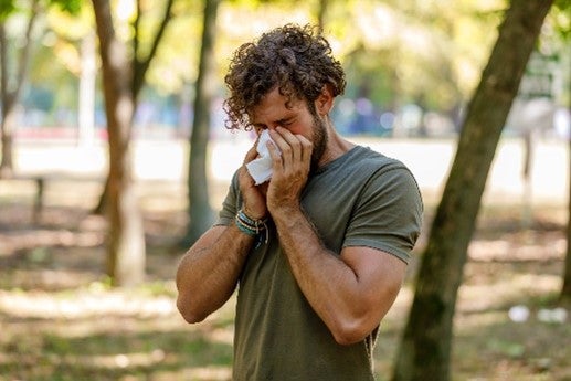 A man in Jupiter, FL, blowing his nose in a park, managing his allergic rhinitis
