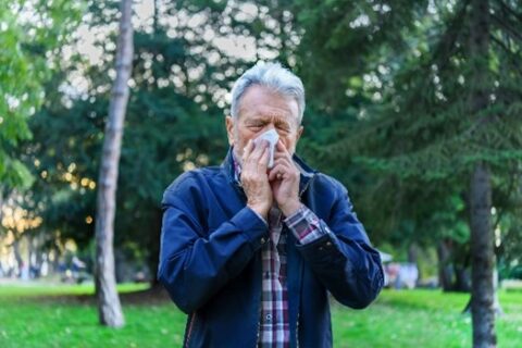 Senior man blowing his nose while sitting on a park bench in Jupiter, FL